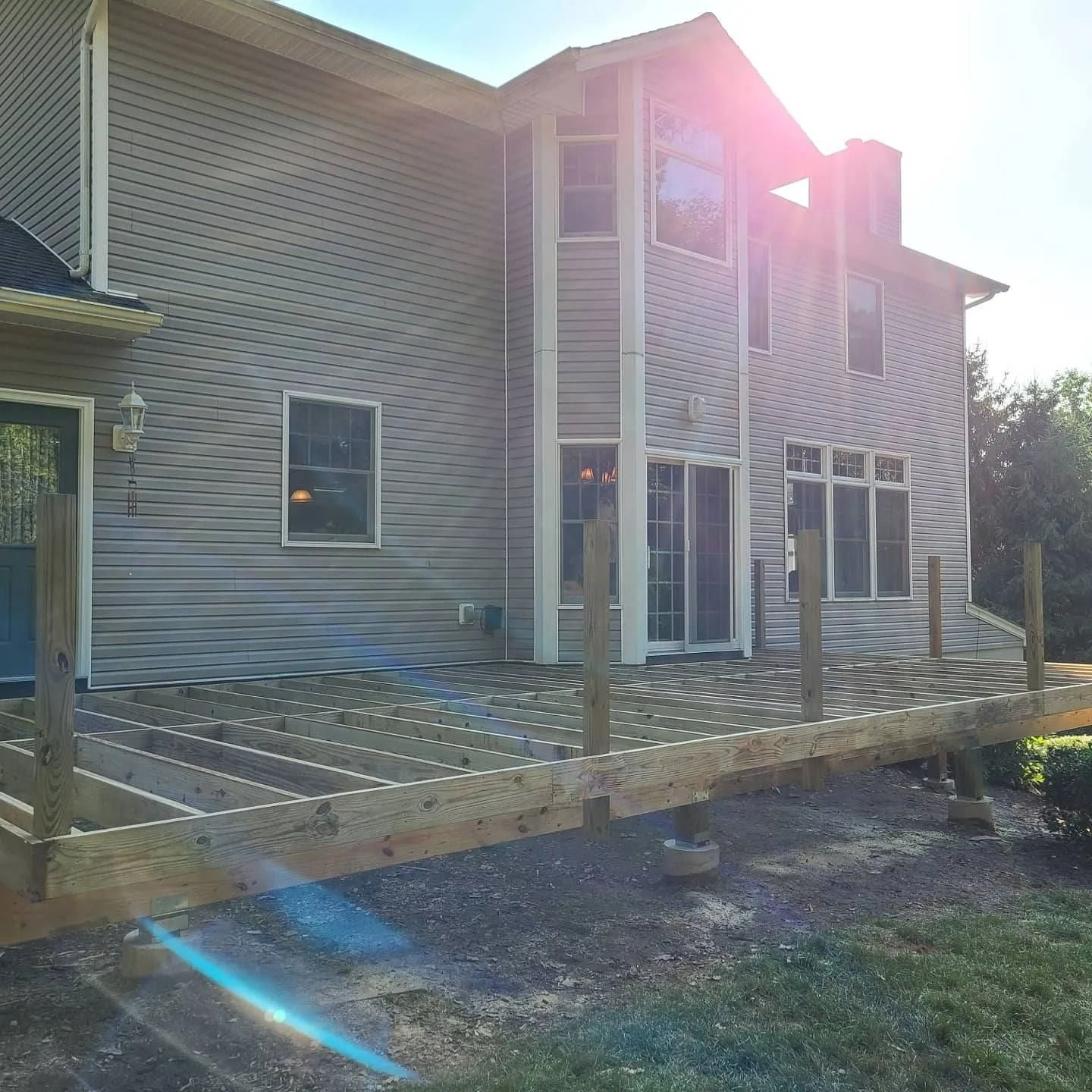Back deck with wooden railing and stairs beside a gray house, lit by bright sunlight