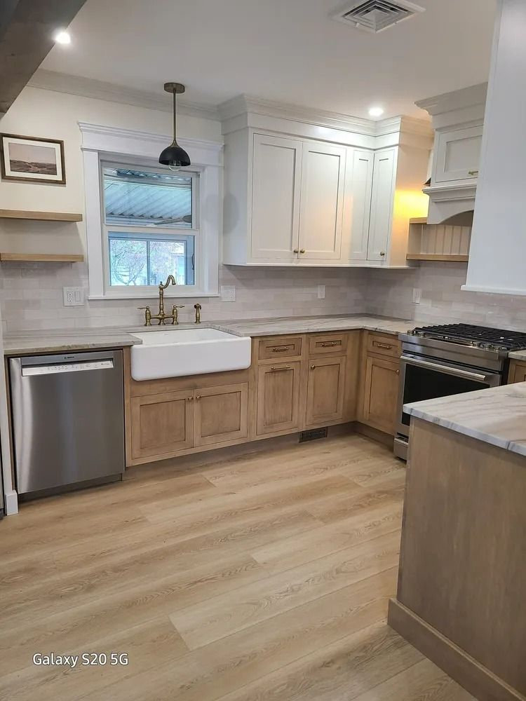 Bright kitchen with white cabinets, farmhouse sink, stainless dishwasher, wood floors, and a black stove.