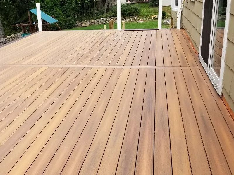Wooden deck patio with horizontal planks beside a house and garden
