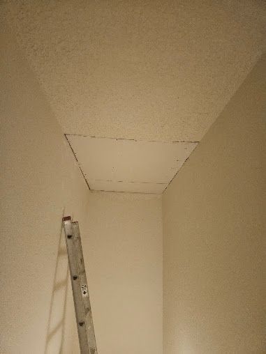 A ladder beneath an open ceiling access panel in a beige room