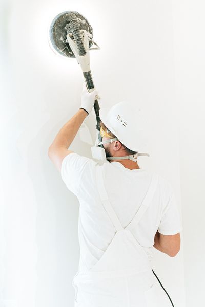 Person in white painting a wall with a roller brush in a bright room
