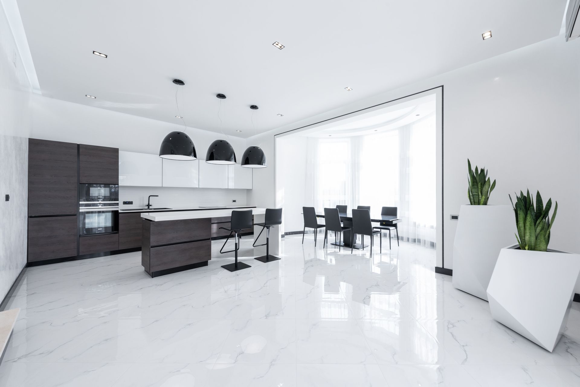 Modern white kitchen and dining area with glossy floors, dark cabinets, and large windows.