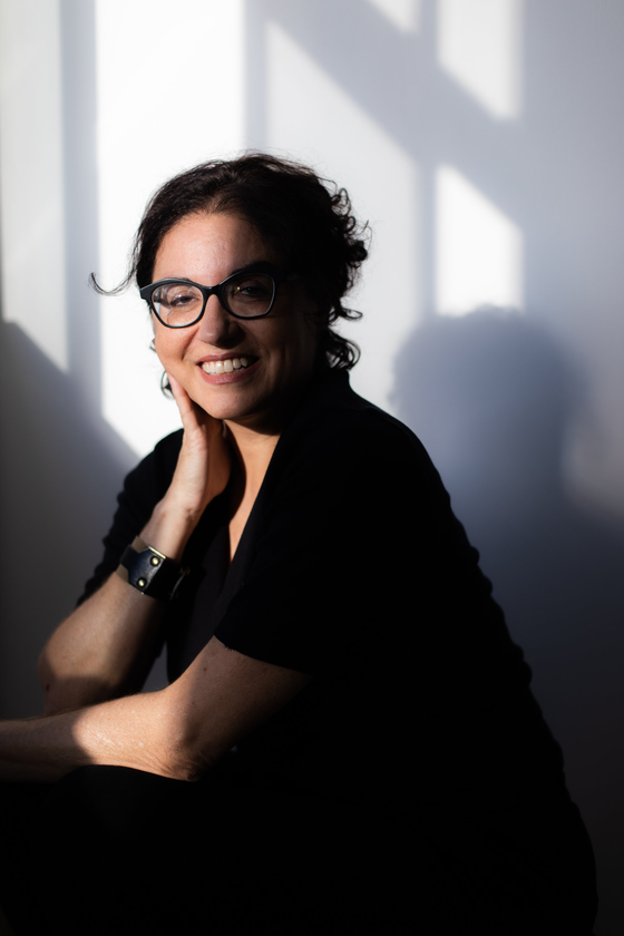 A woman wearing glasses and a black shirt is sitting in front of a window.