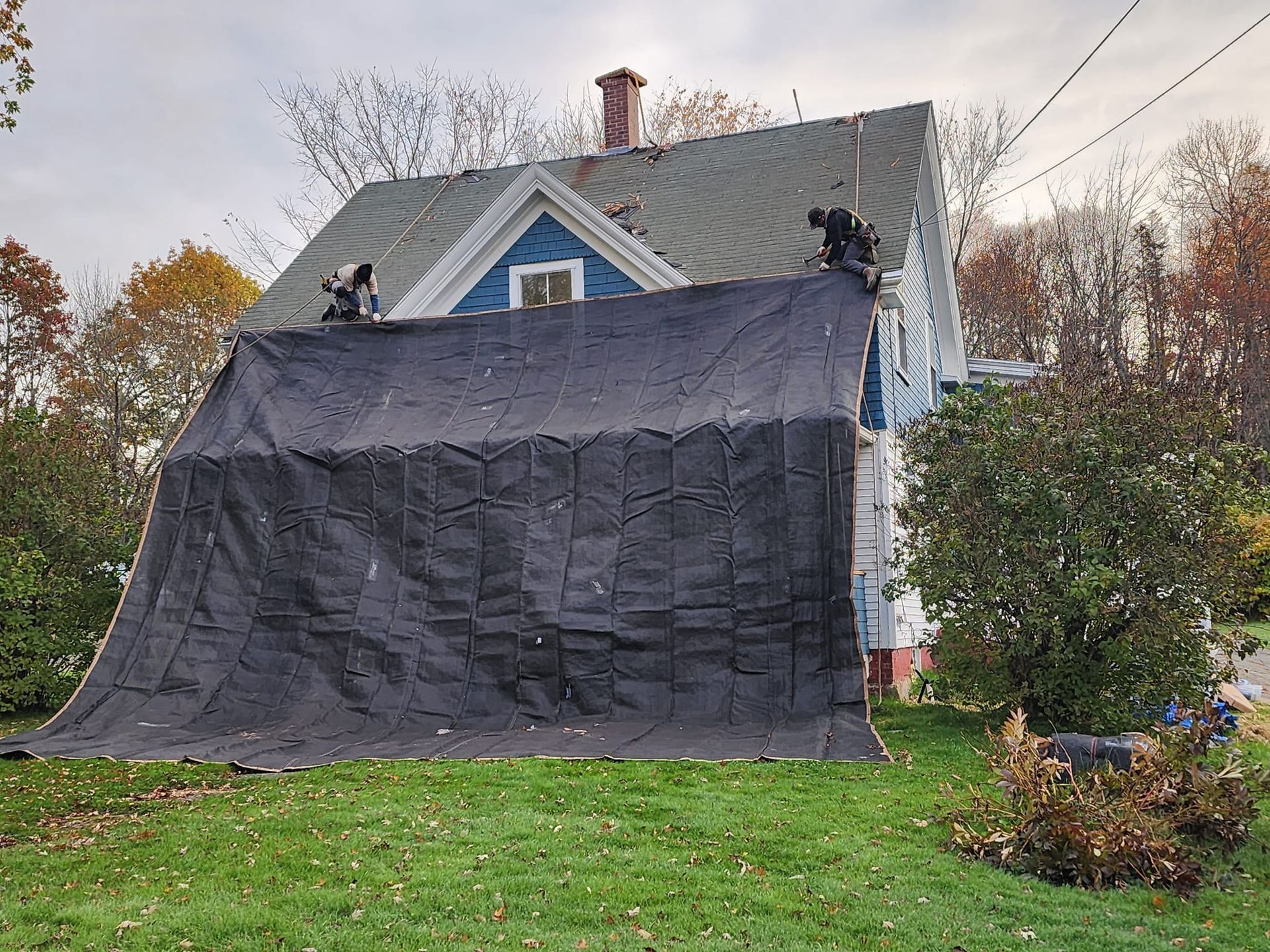 A large black tarp is covering the roof of a house.
