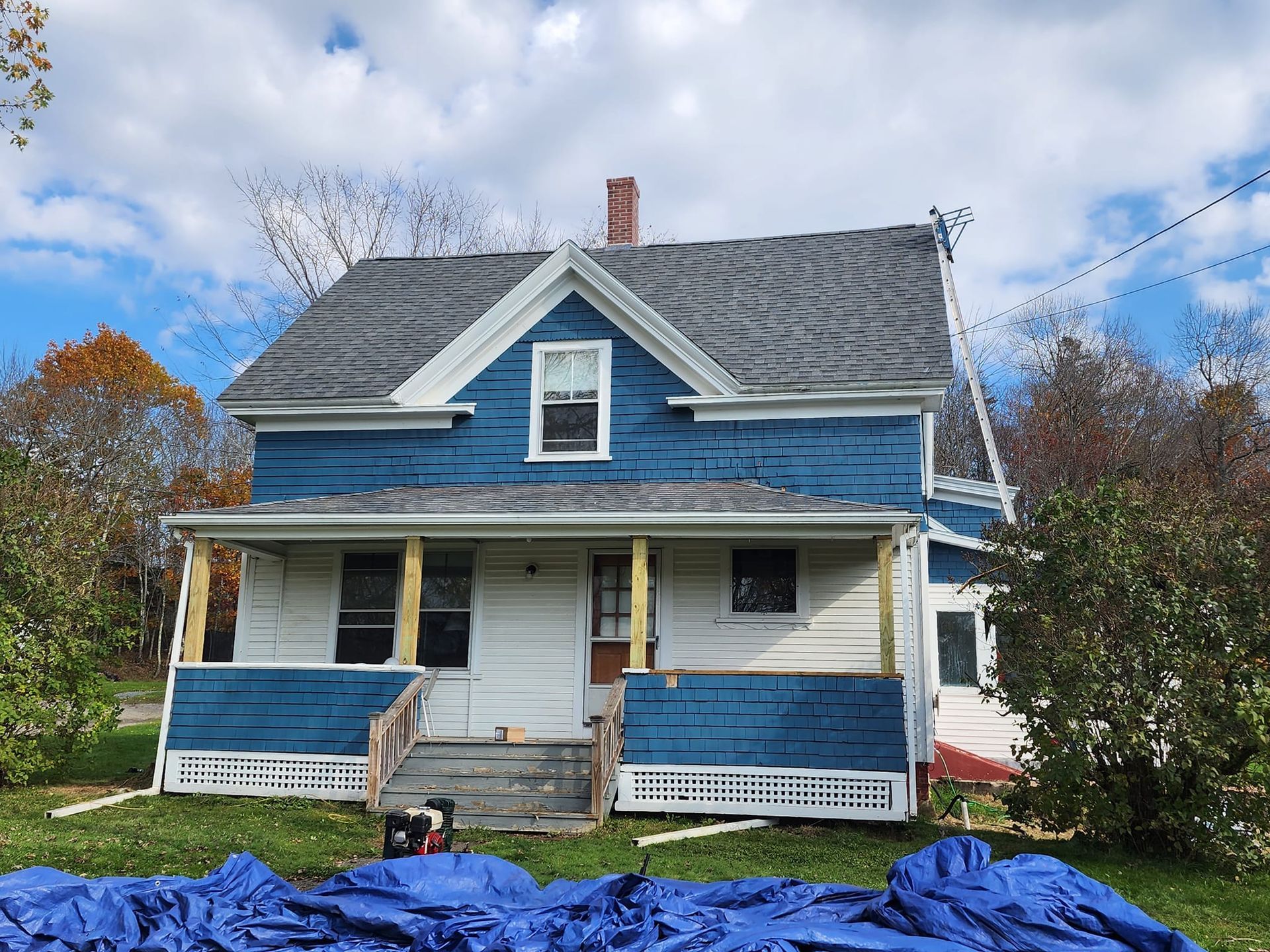 A blue and white house with a blue tarp in front of it.