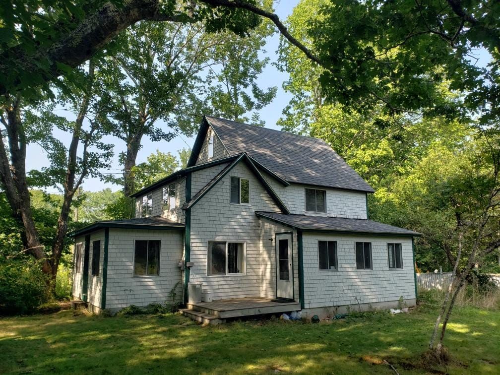 A white house with a black roof is surrounded by trees.