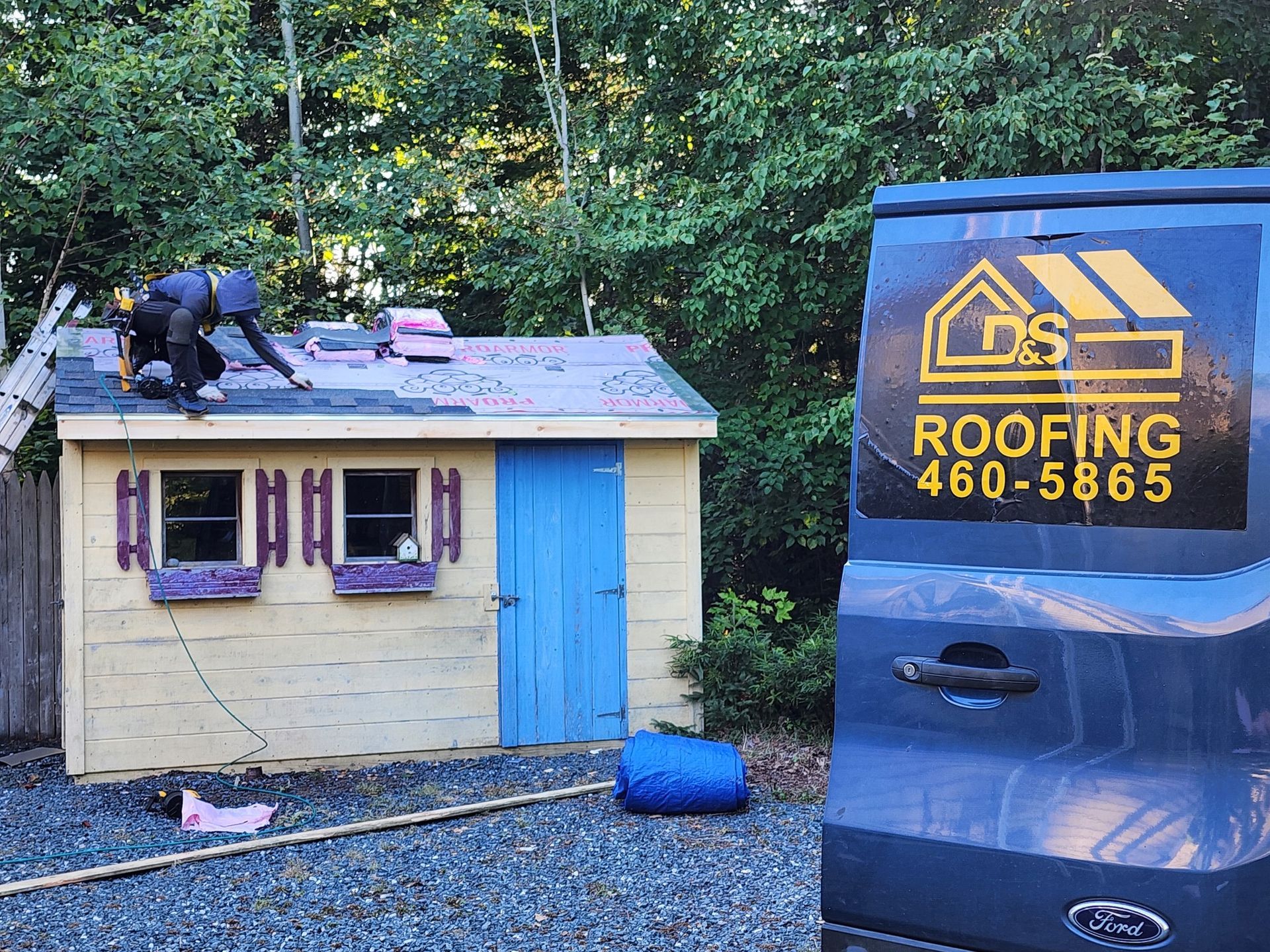 A man is working on the roof of a shed next to a roofing van.