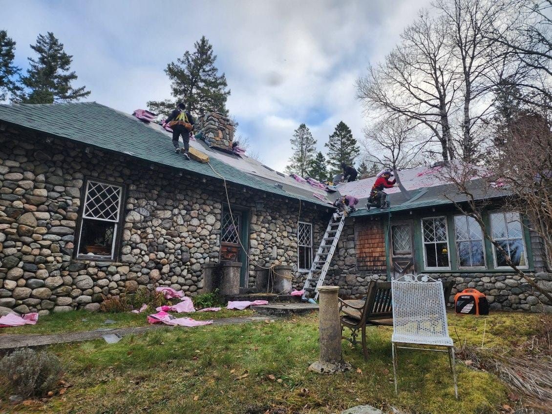 A group of people are working on the roof of a stone house.