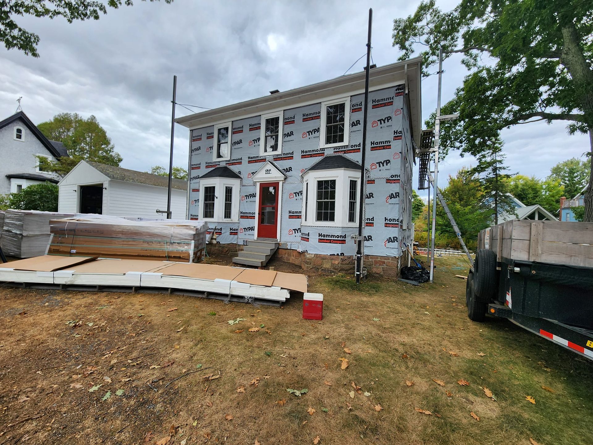A large white house with a red door is being remodeled.
