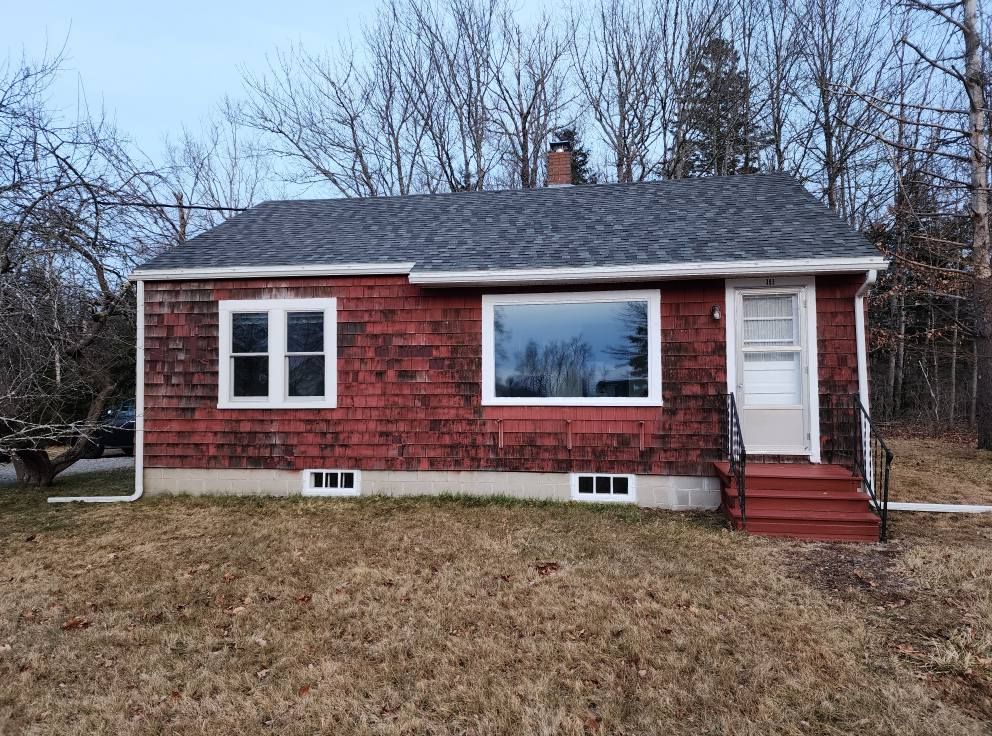 A small red house with a gray roof is sitting in the middle of a grassy field.