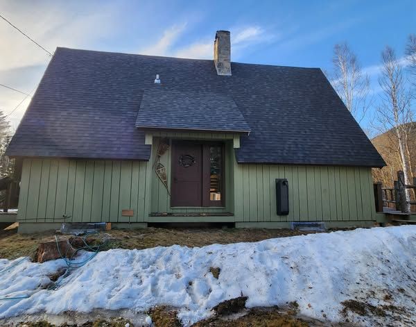 A green house with a black roof is surrounded by snow.