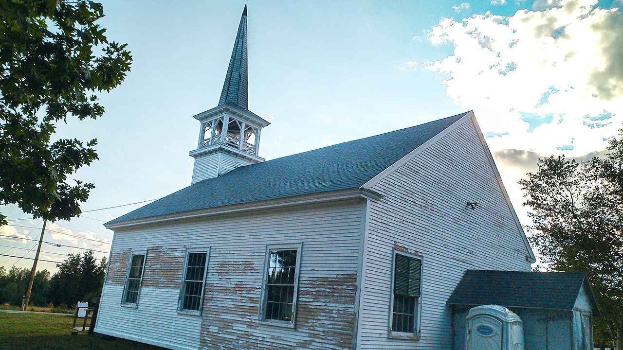 A small white church with a steeple in the middle of a field.
