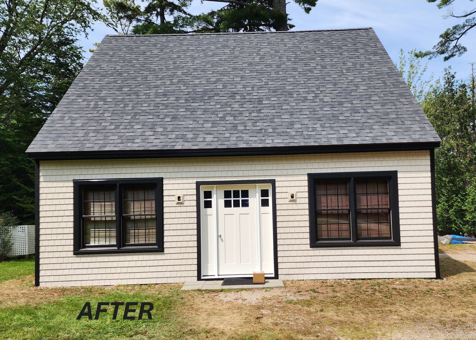 A newly renovated small house with a white door, black-framed windows, and gray roof.