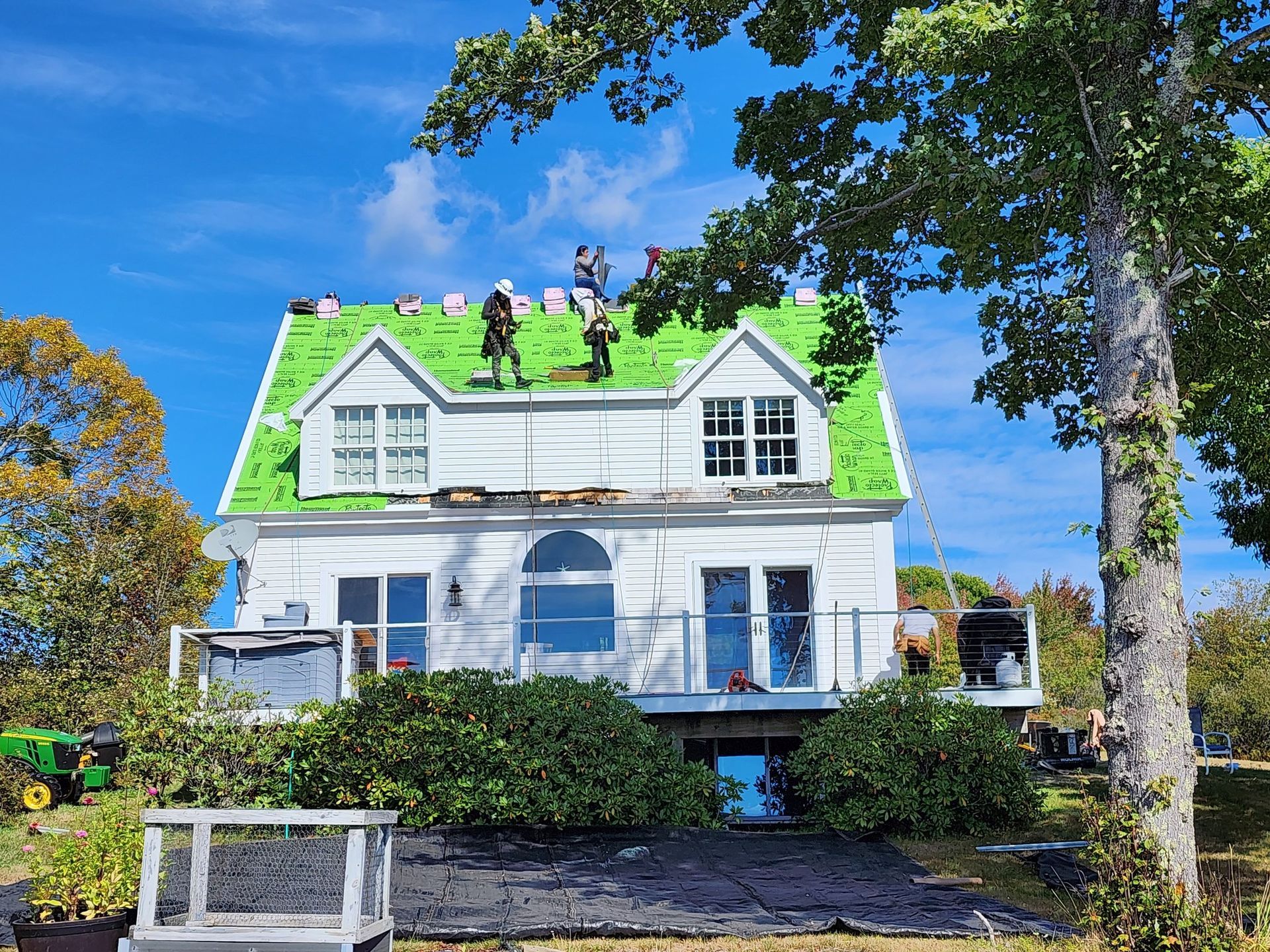 White house with green roof under construction; workers on roof in sunlight.