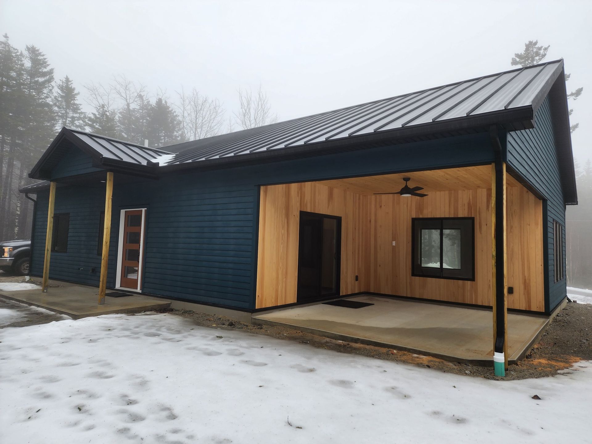 A blue house with a black roof and a porch in the snow.