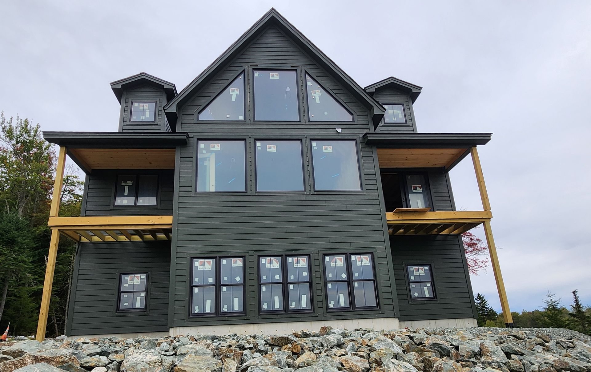 Dark gray house with large windows and two-level decks. Building is on a rocky foundation.