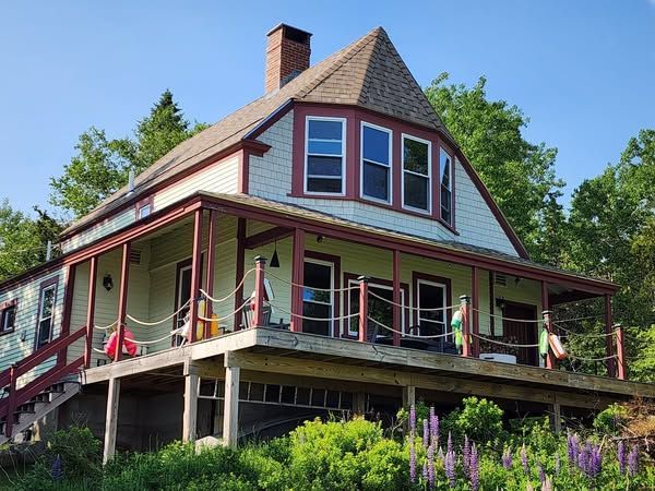 A large house with a large porch is surrounded by trees and flowers.