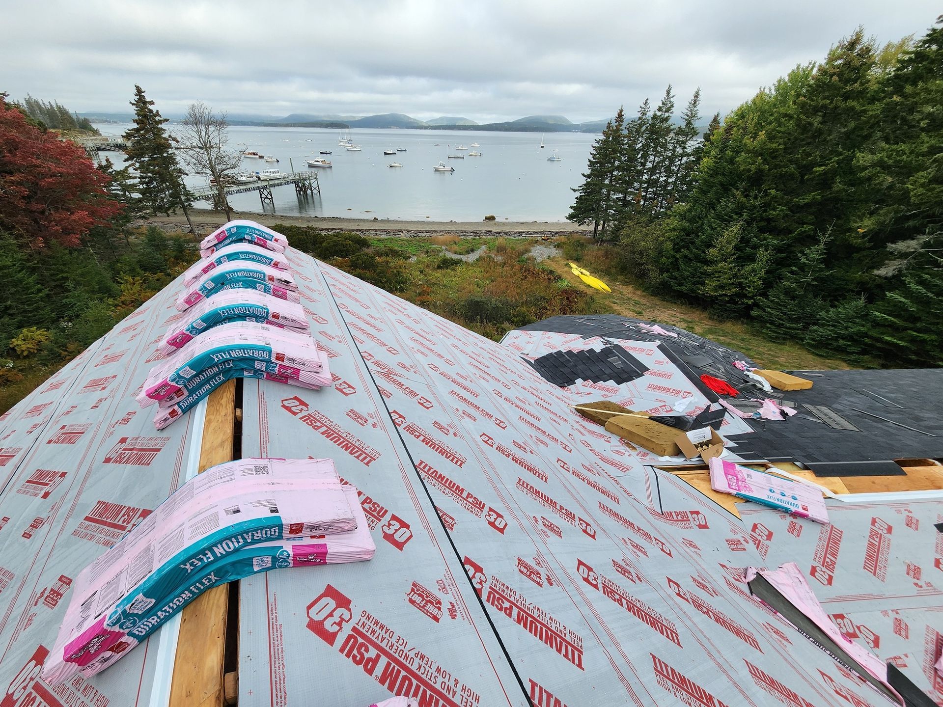 View from a roof under construction featuring ridge vent material and underlayment, overlooking a scenic coastal bay.