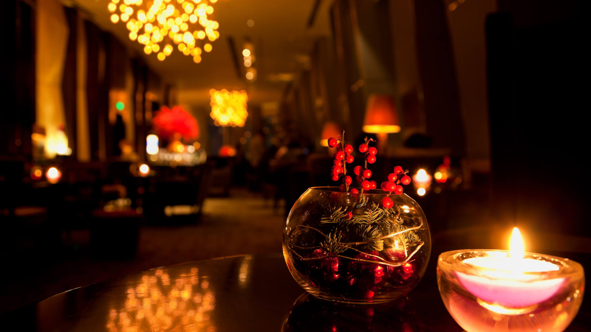 Dimly lit restaurant table with glowing candles and a red floral centerpiece, warm lights in the background