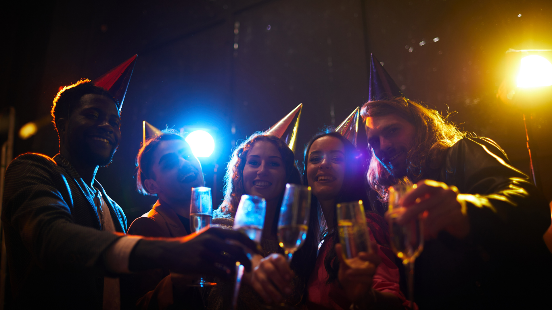 Friends toasting drinks at a dark party, lit by bright blue and yellow lights