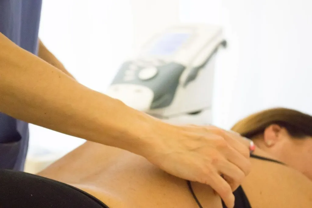 Persona che esegue la fisioterapia sulla schiena di un paziente con un macchinario sullo sfondo.