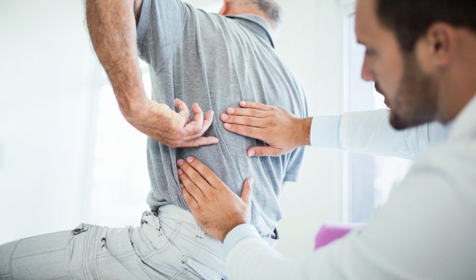 Un medico esamina la parte bassa della schiena di un paziente. Il paziente è piegato in avanti e il medico usa le mani per esaminarlo.