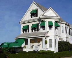 White house with green awnings and a green roof, viewed from the street on a clear day