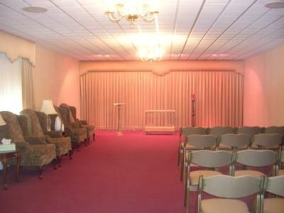Small church hall with rows of chairs facing a curtained stage under pink lighting