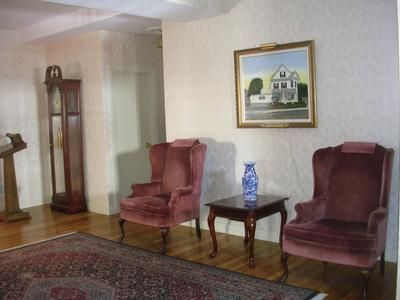 Living room with two burgundy chairs, a small table, rug, clock cabinet, and framed house painting