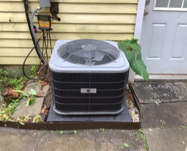 An air conditioning unit sits outside a building. The unit is gray and black with a fan on top.