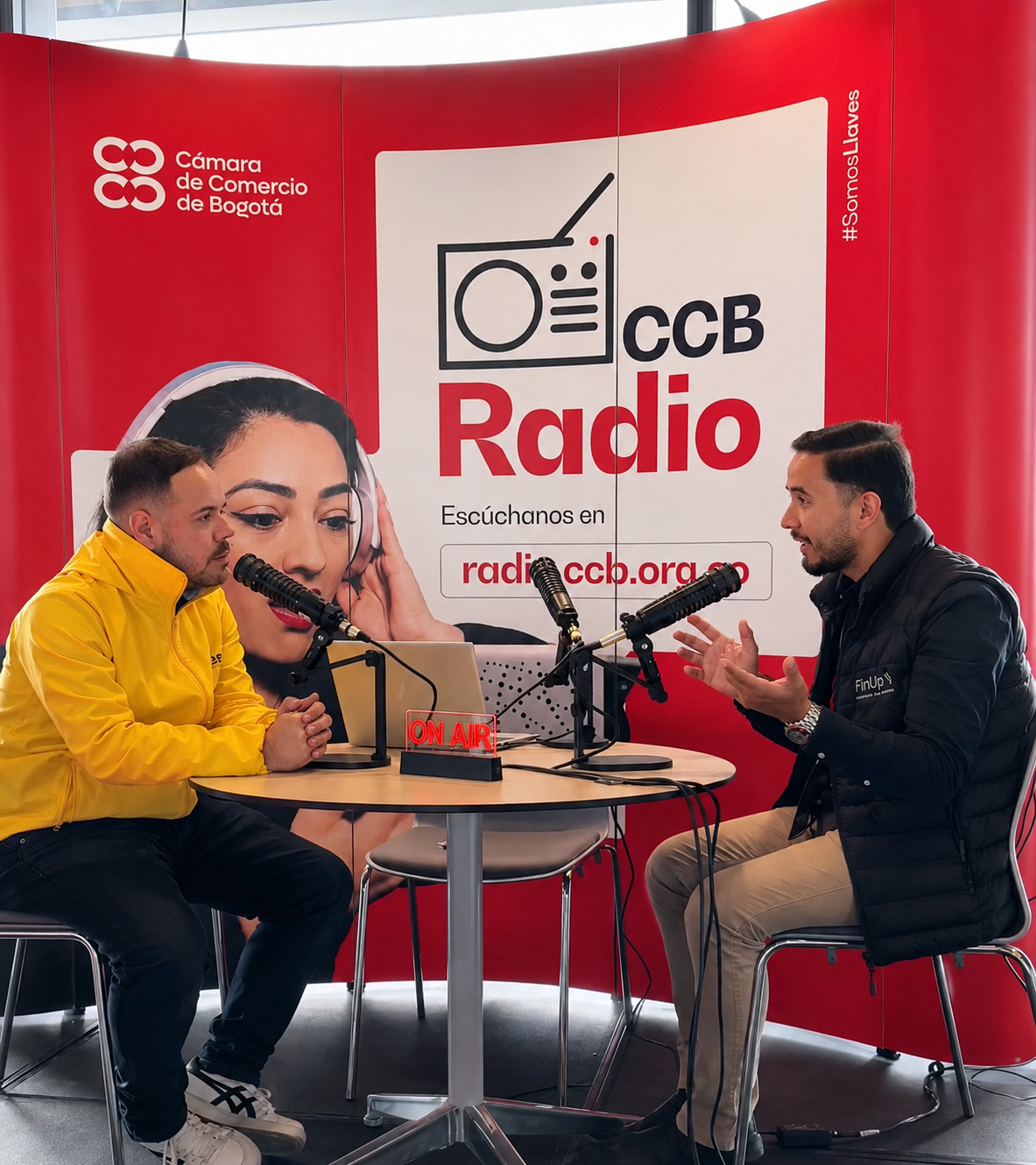 Dos personas graban una entrevista de radio en un estudio rojo de CCB Radio con micrófonos y auriculares.