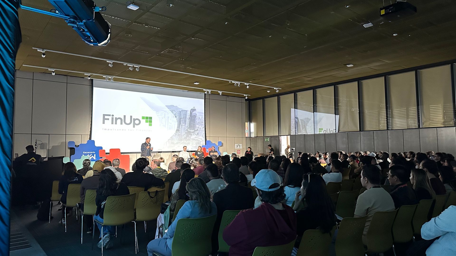 El público de la conferencia se encuentra frente a un escenario donde se proyecta una presentación de FinUp! en una gran pantalla.