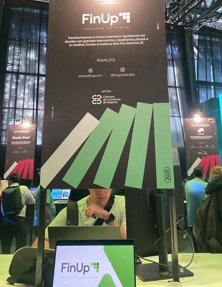 Stand de FinUp con paneles de visualización geométricos verdes y pantallas digitales en una feria comercial.