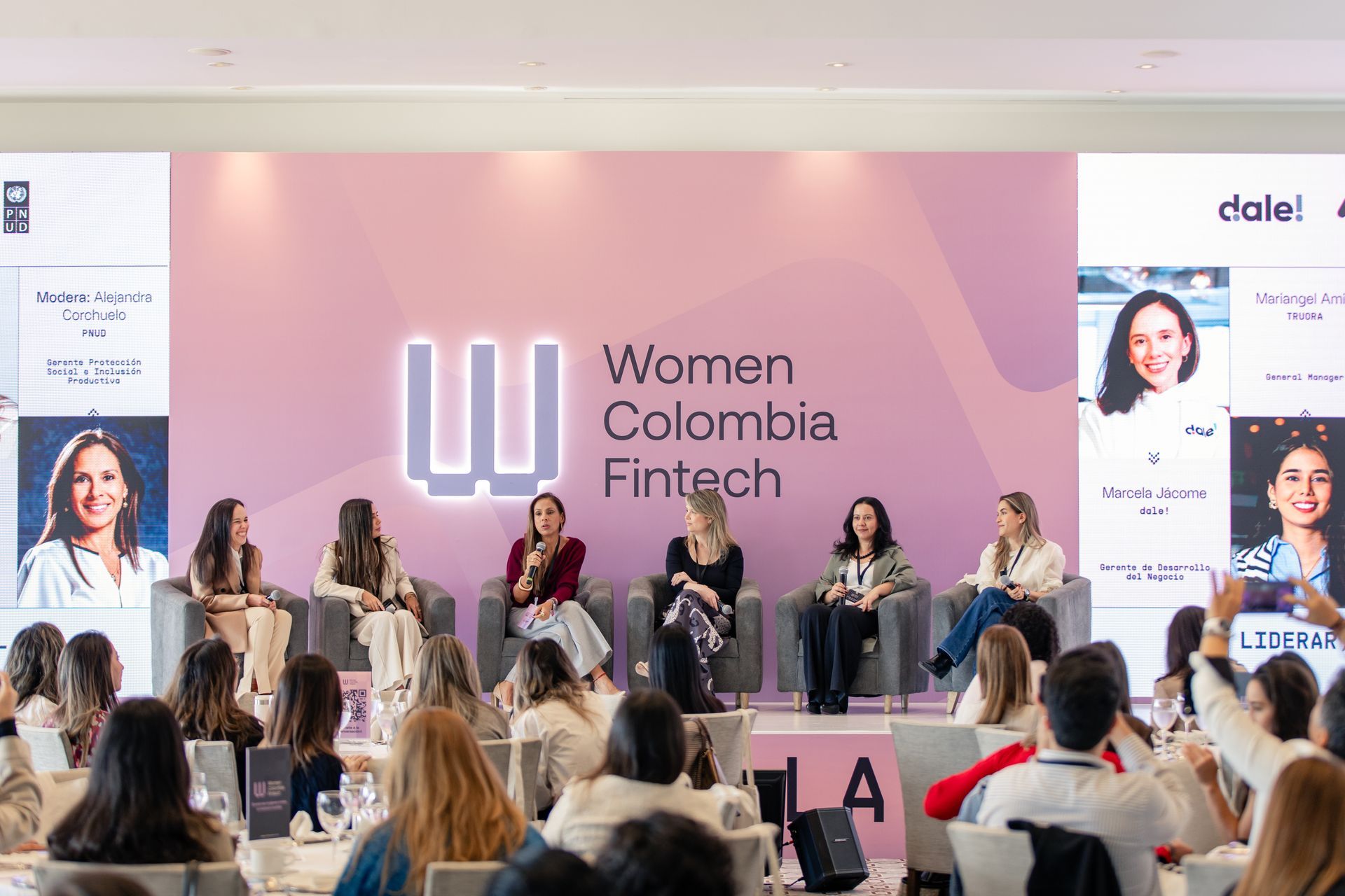 Panel de mujeres colombianas del sector Fintech en un escenario rosa, con ponentes y público al frente.