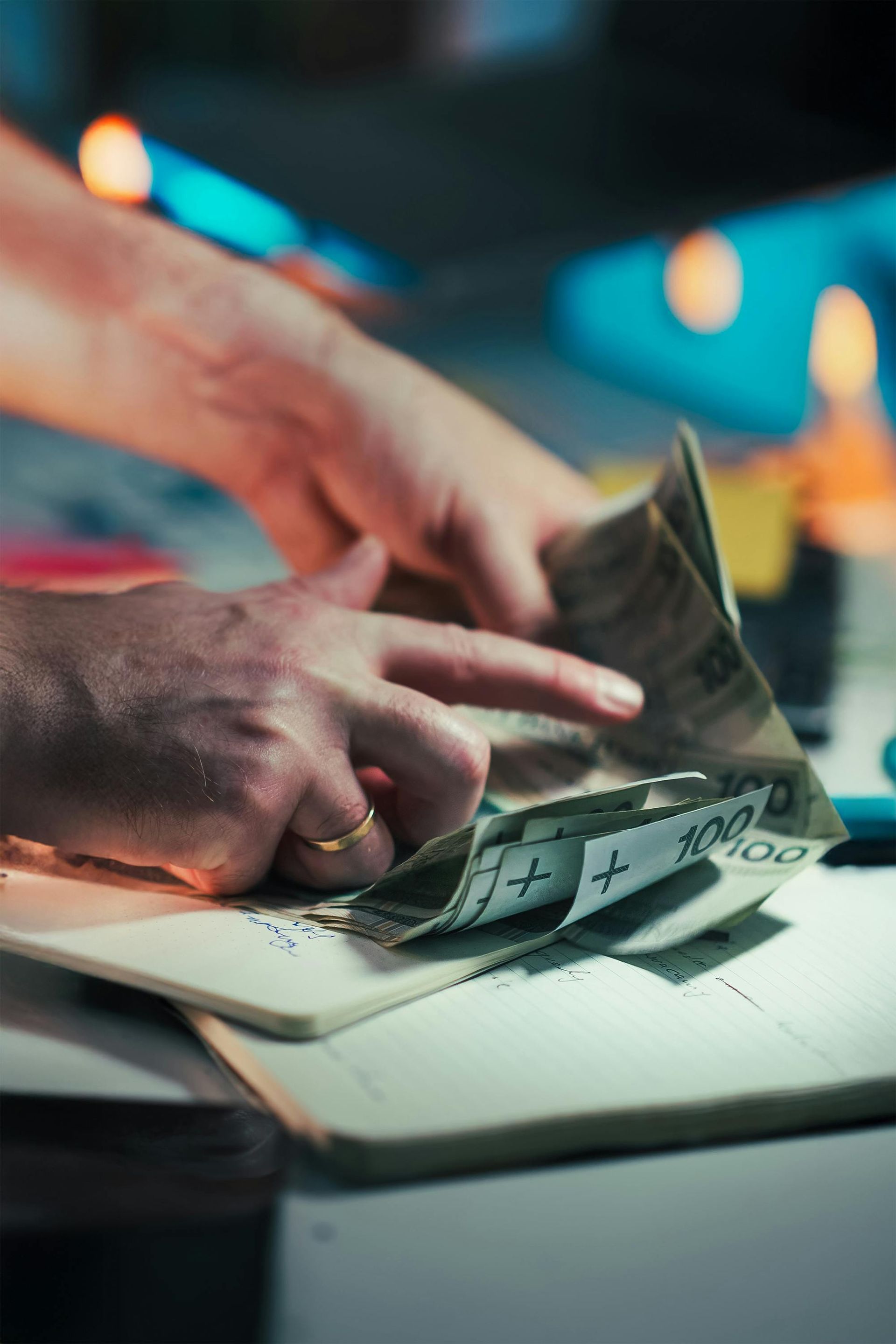 Manos contando dinero en efectivo sobre una mesa iluminada con varios billetes a la vista.