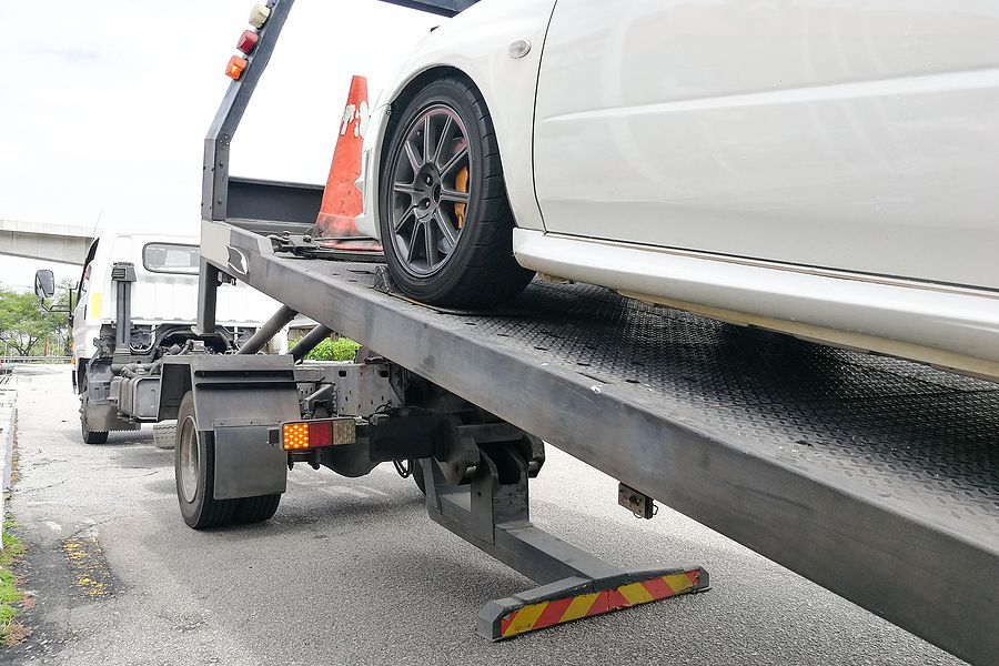 White car being loaded onto a flatbed tow truck.