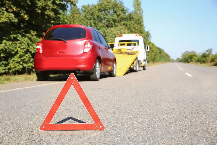 Red car broken down on highway with emergency warning triangle.