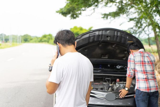 Two men inspecting the engine of a stalled car on the shoulder.
