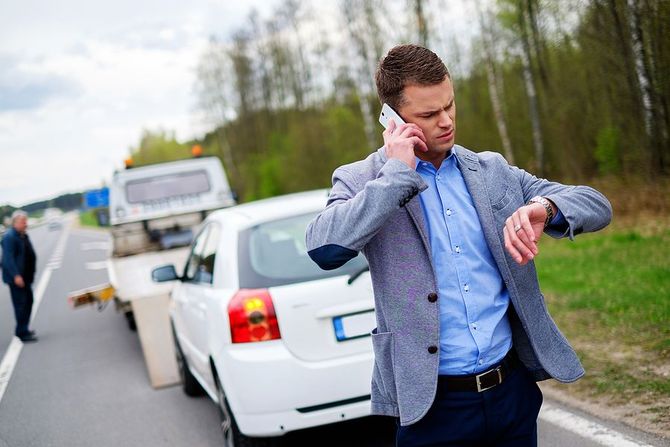 Stressed man checking watch while car is loaded on a tow truck.
