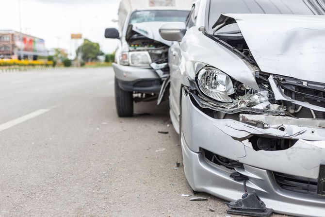 Front-end collision between two silver cars on a city road.
