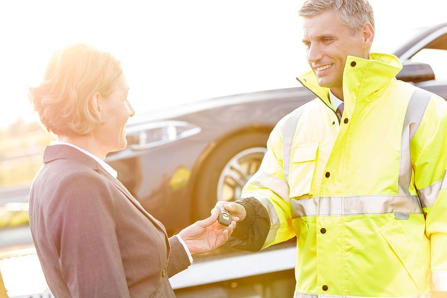 Smiling tow truck driver handing keys to a female customer.
