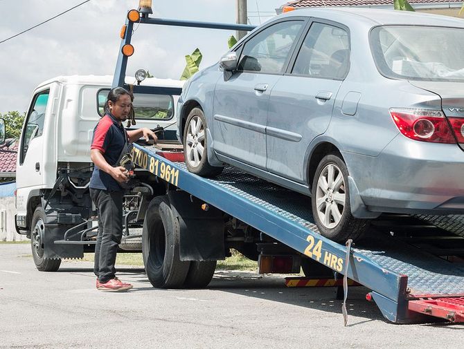 Silver sedan being lifted by a wheel-lift tow truck.