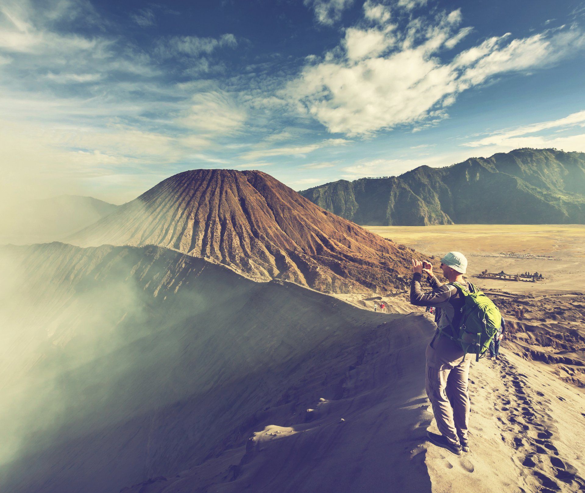 Seorang pria dengan ransel sedang memotret gunung berapi.