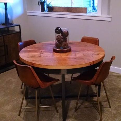 A round wooden table with a vase of pine cones on top
