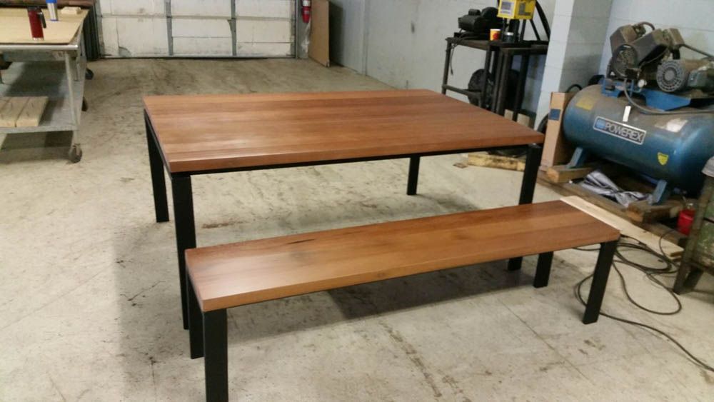 A reclaimed table and bench are in a garage next to a blue air compressor.