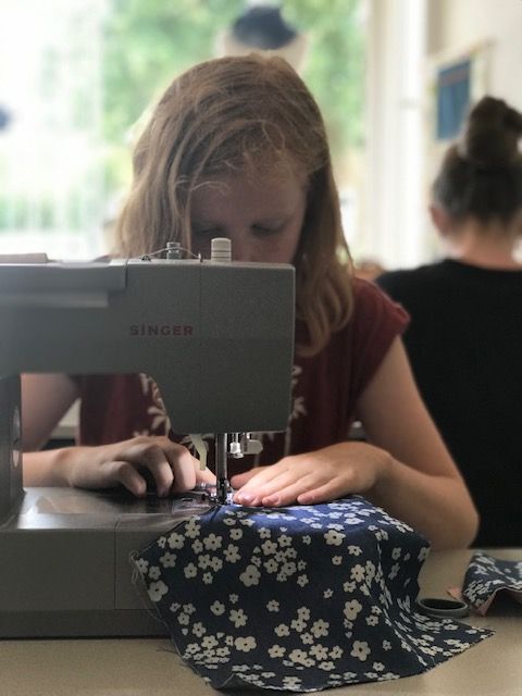 Meisje naait met een Singer naaimachine aan een blauwe stof met bloemenprint.