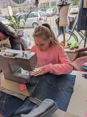 Meisje in een roze trui gebruikt een naaimachine om een spijkerbroek te repareren in een winkel.