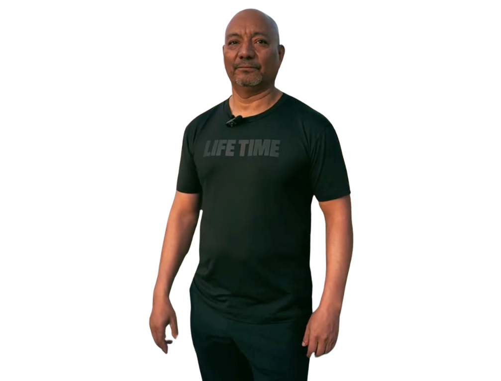 A man wearing a black life time t-shirt is standing in front of a white background.