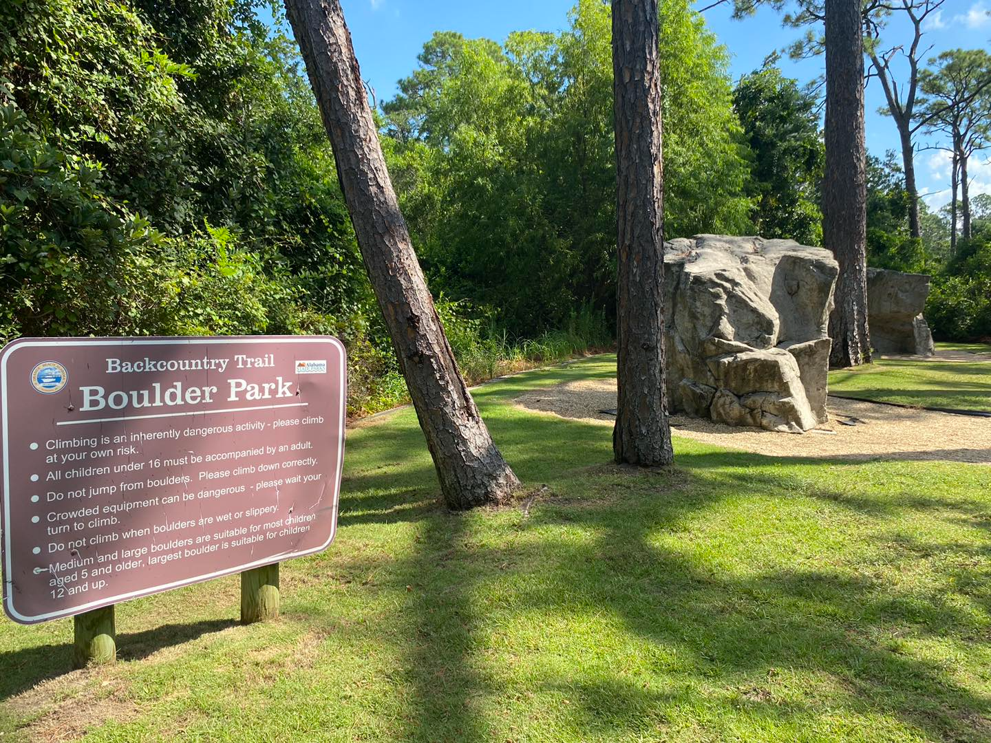 A sign for boulder park is sitting in the grass next to a large rock.
