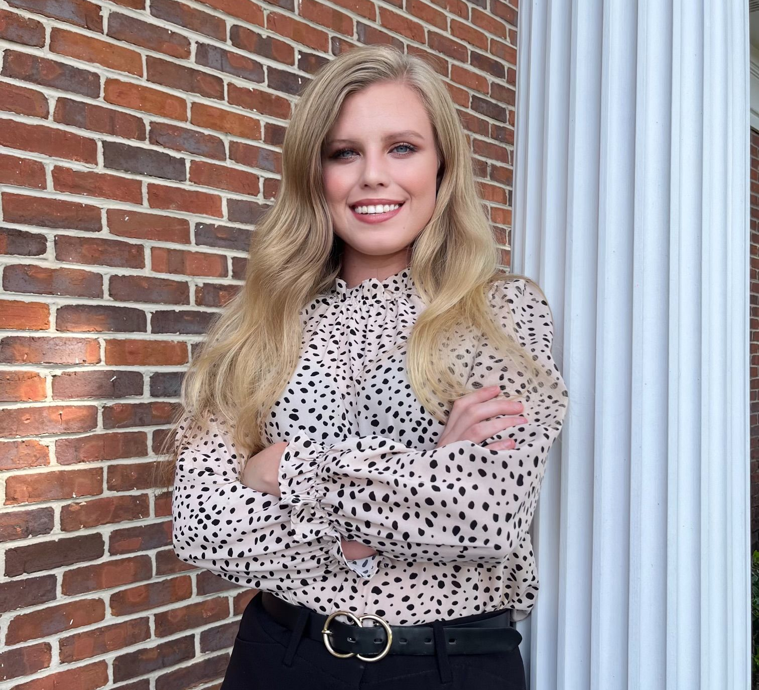 A woman wearing a tan jacket and a black shirt is smiling for the camera.